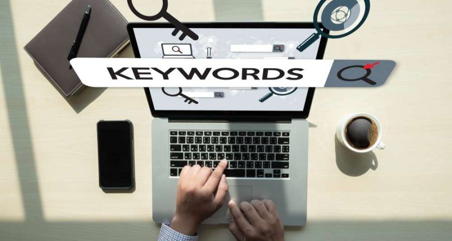 A person performing keyword research using a laptop with their phone next to them