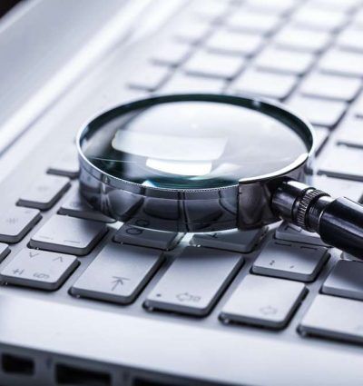 A side view of a keyboard with a magnifying glass on top, used to symbolize search results.