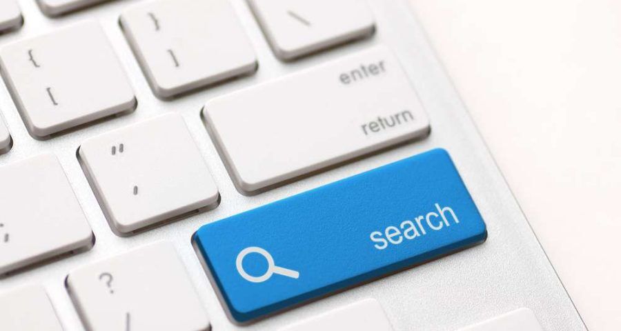 A closeup image of a Macbook keyboard. The white enter key can be seen above a blue key labeled "search", with a magnifying glass next to it.