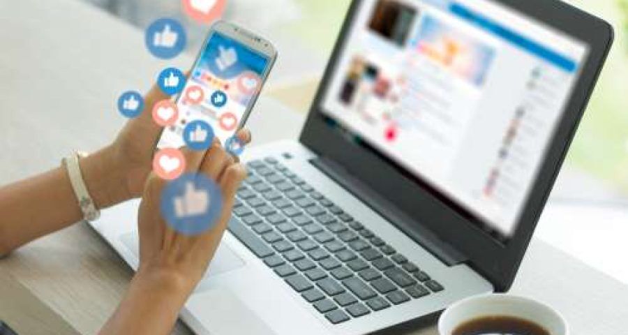 open laptop with person on iphone scrolling through social media