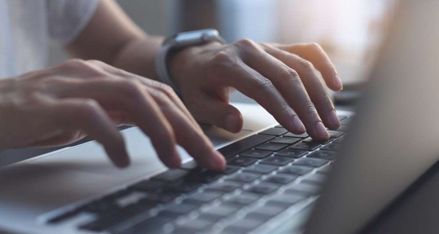 A closeup of a man's hands typing away on a laptop's keyboard.