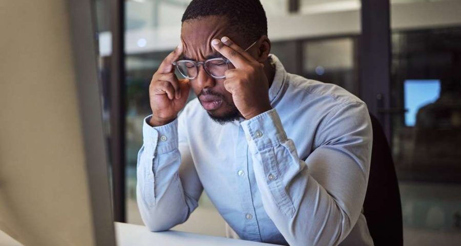 Stressed business man with blue buttoned shirt in front of his computer with his fingers on his head
