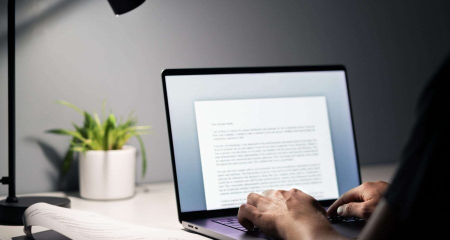 man writing content on a document with his laptop