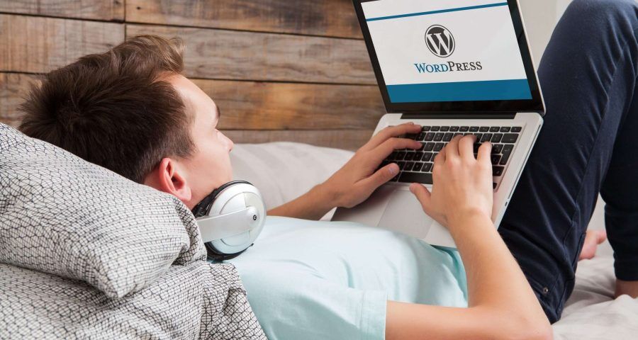 A relaxed individual comfortably checks their WordPress version while lying on a bed with a laptop, depicting the ease of managing a WordPress site from anywhere.